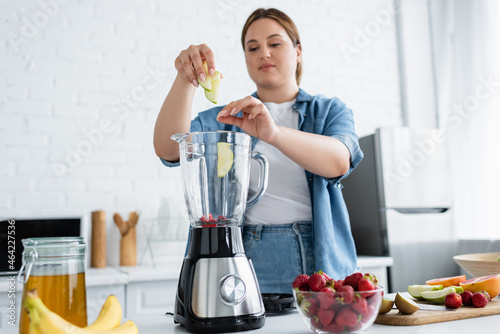 Blurred woman with overweight cooking smoothie in blender in kitchen