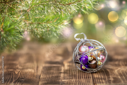 Christmas ornament lies under the Christmas tree on a wooden surface. Defocused lights in the background