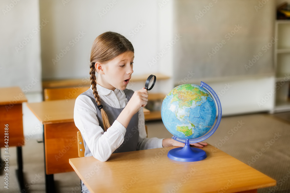 Surprised preteen schoolgirl with long hair in pigtails at a desk with a globe, schoolgirl shows studying a map of the world, the concept of school and travel Surprised preteen schoolgirl with long hair in pigtails at a desk with a globe, schoolgirl shows studying a map of the world, the concept of school and travel