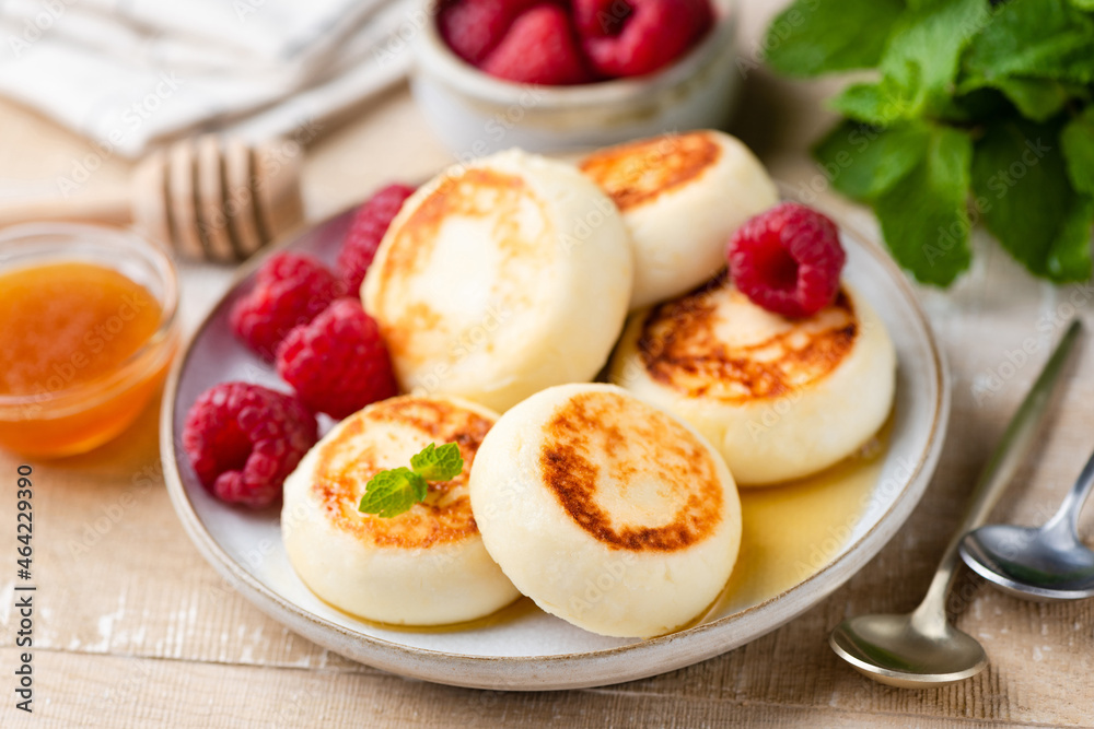Cheese fritters, pancakes or syrniki with honey on a wooden table background served with fresh raspberries, closeup view Cheese fritters, pancakes or syrniki with honey on a wooden table background served with fresh raspberries, closeup view
