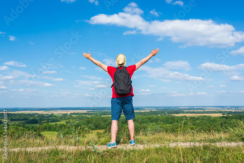 Tourist man with backpack enjoying the view in nature.Traveler man with backpack,arms outstretched stand on blue sky.