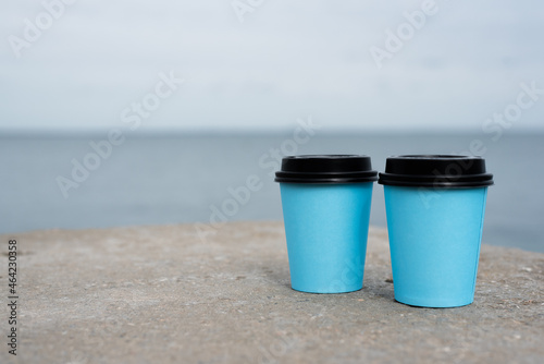 Two coffee cups on the ground close up on the sea water background. © Natali