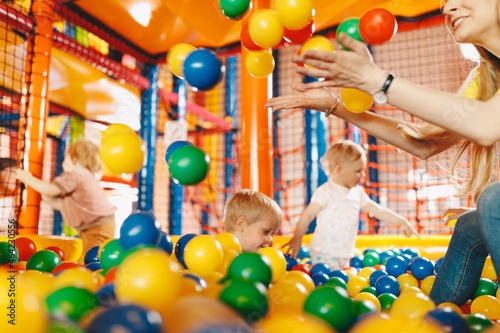 Happy kids playing in amusement park balls pool with young teacher. Kids cheering and ​playing with plastic colourful balls. Children throwing balls high. Playing with balls: activities for childre photo