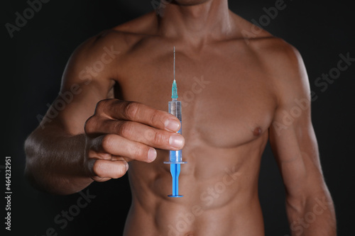 Athletic man with syringe against black background, closeup. Doping concept