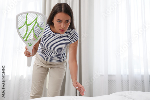 Billede på lærred Young woman with electric fly swatter in bedroom. Insect killer