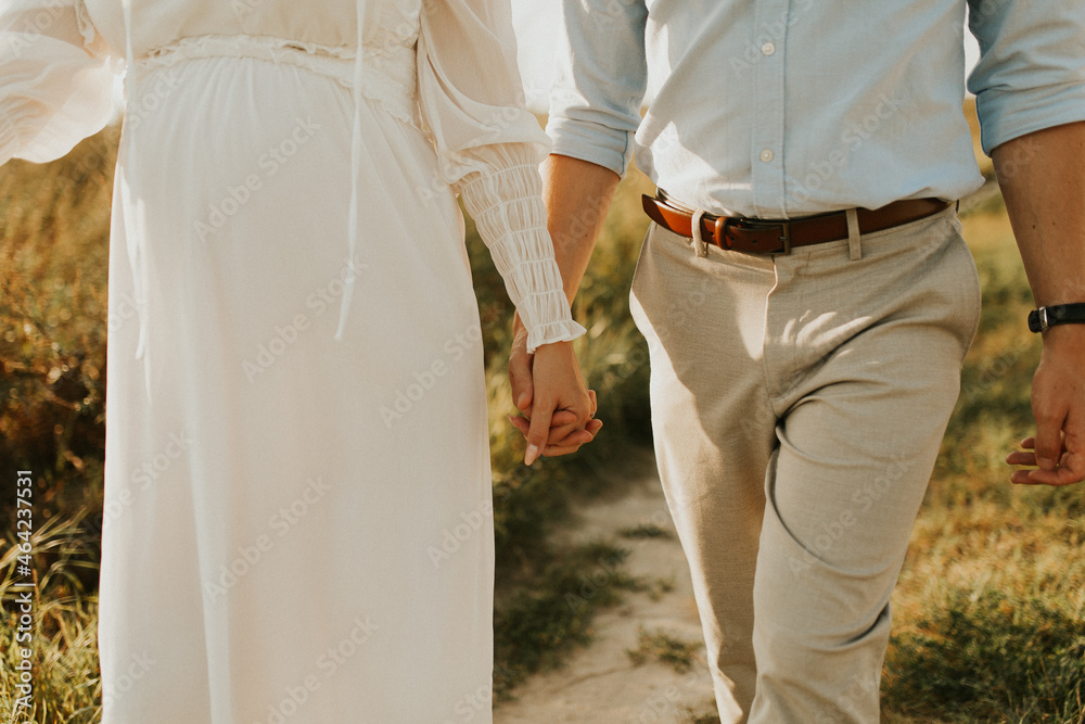 The spirit of love, freedom and independence. Happy young couple in love running in the field in the sunset light.  Freedom and love concept. Close up of holding hands. Pregnant woman
