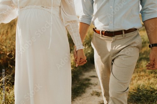 The spirit of love, freedom and independence. Happy young couple in love running in the field in the sunset light. Freedom and love concept. Close up of holding hands. Pregnant woman 