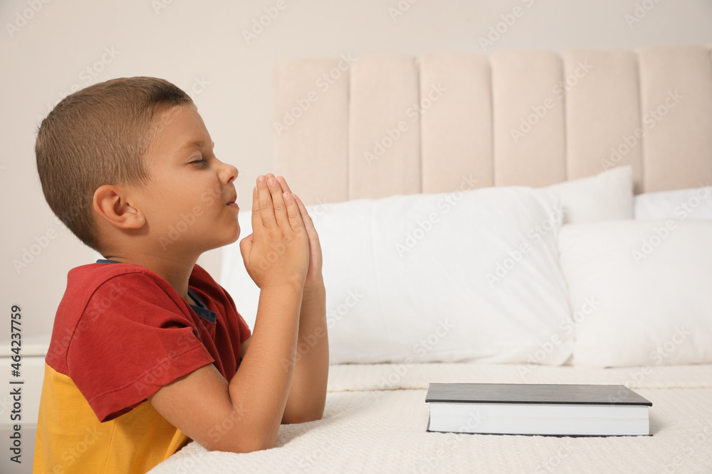 Cute little boy with hands clasped together saying bedtime prayer over Bible at home. Space for text Cute little boy with hands clasped together saying bedtime prayer over Bible at home. Space for text