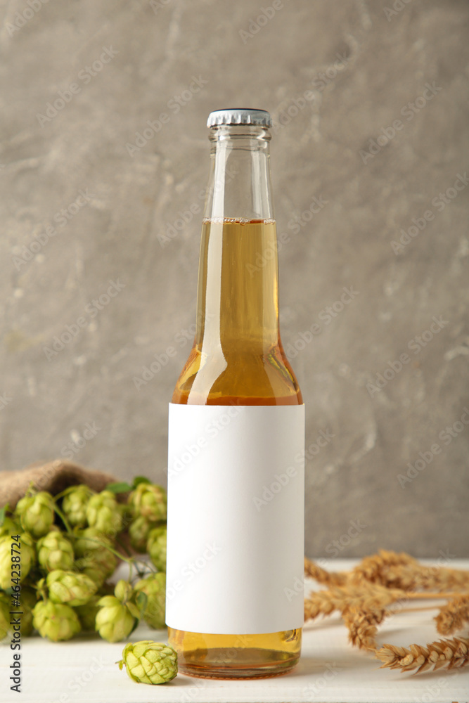 Beer bottle with hop cones and wheat on grey background, close up.
