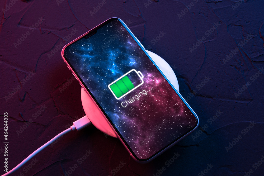 Mobile smart phone on wireless charging device on dark neon red and blue color background. Icon battery and charging progress lighting on screen.smartphones connected to power source.Low battery - obrazy, fototapety, plakaty 