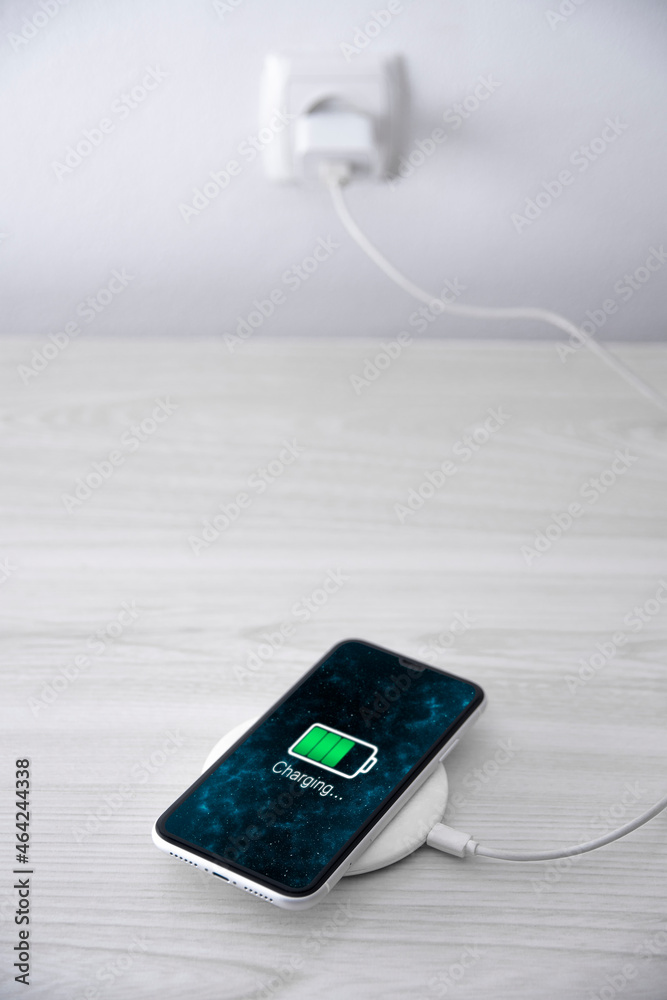 Mobile smart phone on wireless charging device on white background. Icon battery and charging progress lighting on screen.smartphones connected to power source.low battery level problems.Plugged Phone Mobile smart phone on wireless charging device on white background. Icon battery and charging progress lighting on screen.smartphones connected to power source.low battery level problems.Plugged Phone