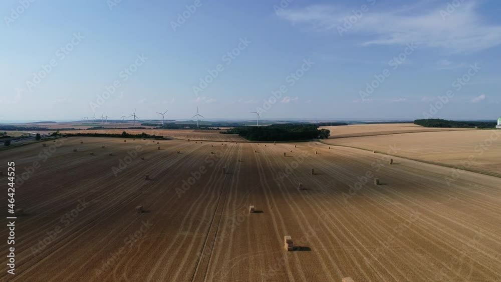 Large wind turbines with blades in field aerial view bright orange sunset blue sky wind park slow motion drone turn. Silhouettes windmills, large orange sun disc summer lens flare. Alternative energy