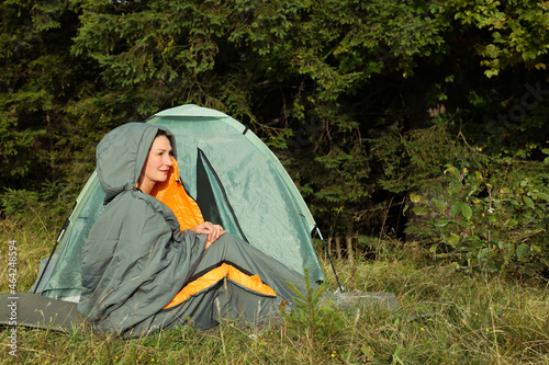 Mature woman in sleeping bag near camping tent outdoors