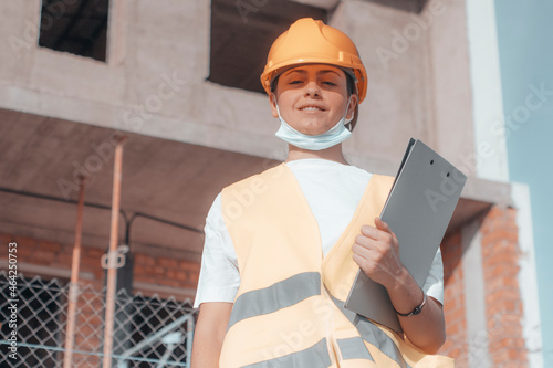 Mujer joven arquitecta de obra trabajando en una reconstrucción para una inmobiliaria junto con su carpeta de trabajo y casco de protección  photo