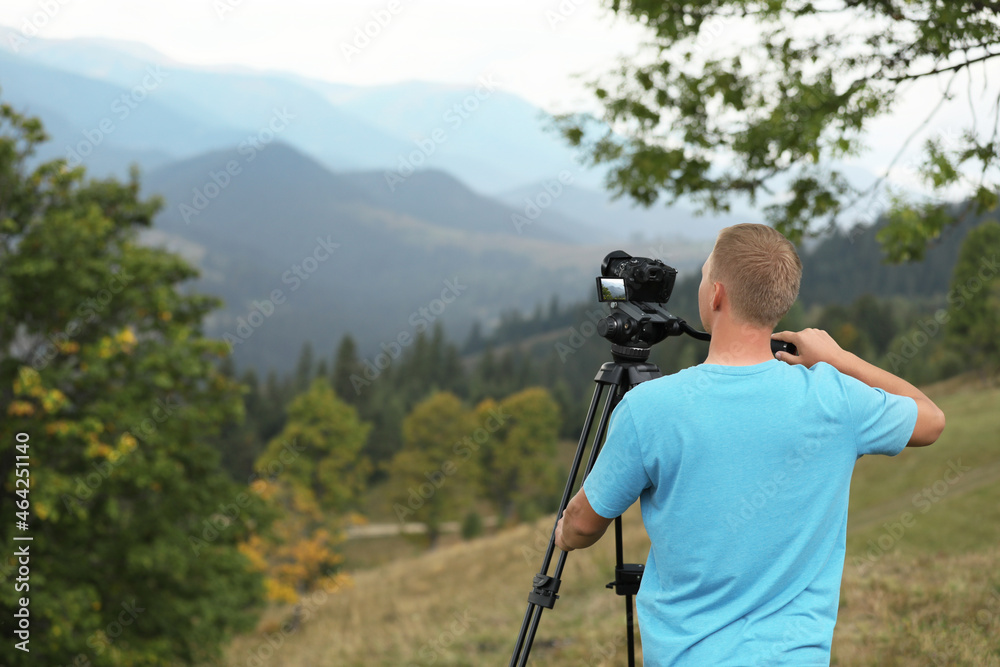 Photographer taking video with modern camera on tripod in mountains Photographer taking video with modern camera on tripod in mountains