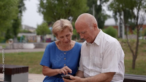 A happy elderly couple of pensioners, holding a smartphone in their hands, looks at the mobile phone screen and looks at funny photos. The older grandparents of the family are having fun