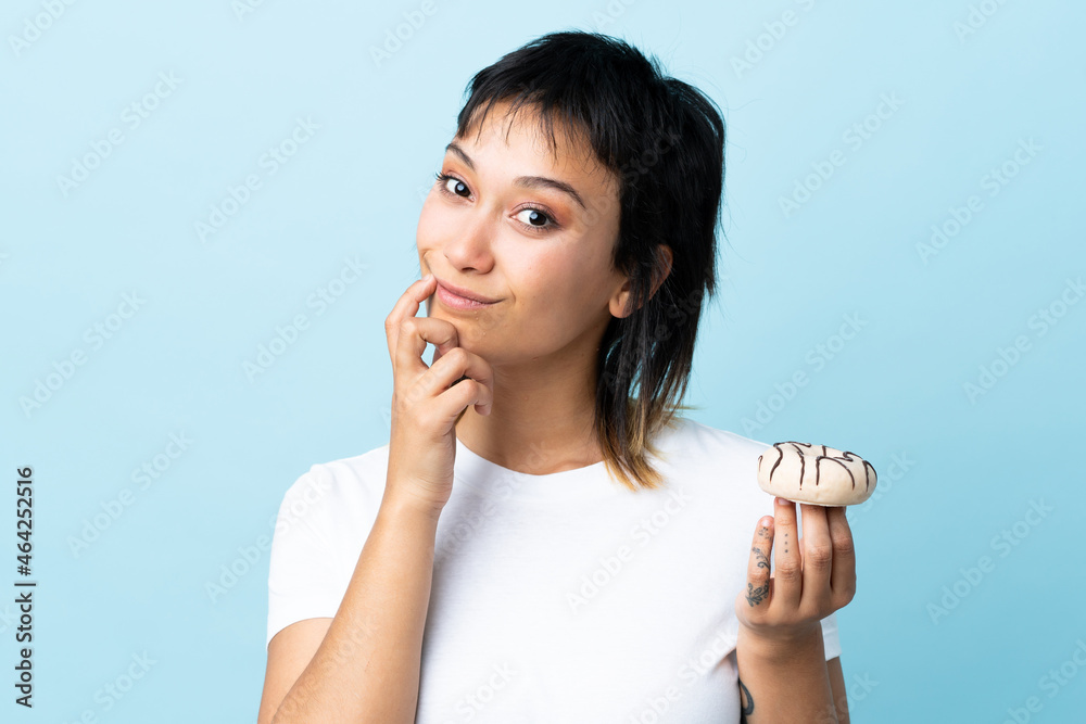 Young Uruguayan woman over isolated blue background holding a donut Young Uruguayan woman over isolated blue background holding a donut