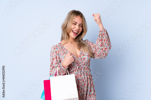 Teenager Russian girl with shopping bag isolated on blue background celebrating a victory