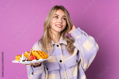 Teenager Russian girl holding waffles isolated on purple background thinking an idea