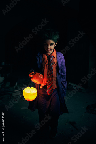 Boy in trickster costume with glowing pumpkin in darkness photo