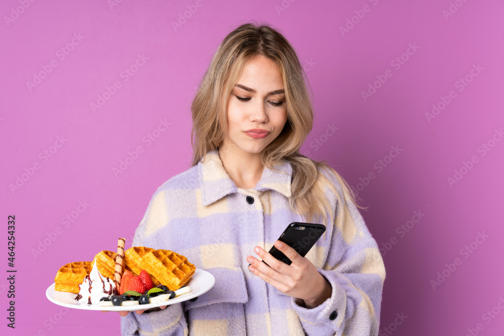 Teenager Russian girl holding waffles isolated on purple background thinking and sending a message Teenager Russian girl holding waffles isolated on purple background thinking and sending a message