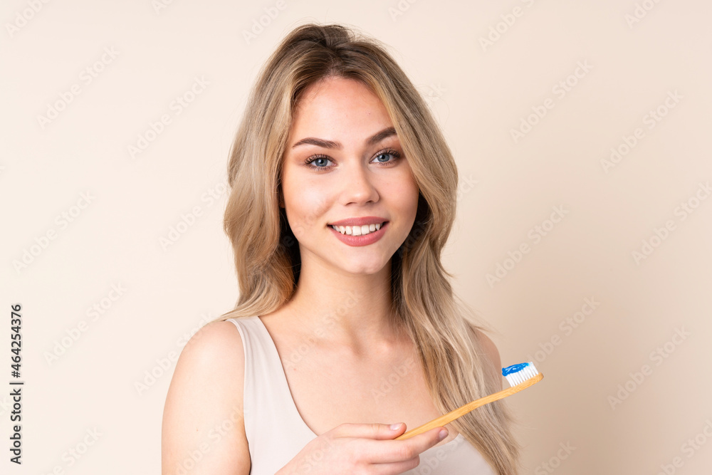 Teenager blonde girl brushing her teeth over isolated background Teenager blonde girl brushing her teeth over isolated background
