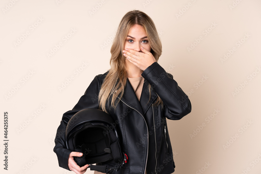 Russian girl with a motorcycle helmet isolated on beige background covering mouth with hands Russian girl with a motorcycle helmet isolated on beige background covering mouth with hands
