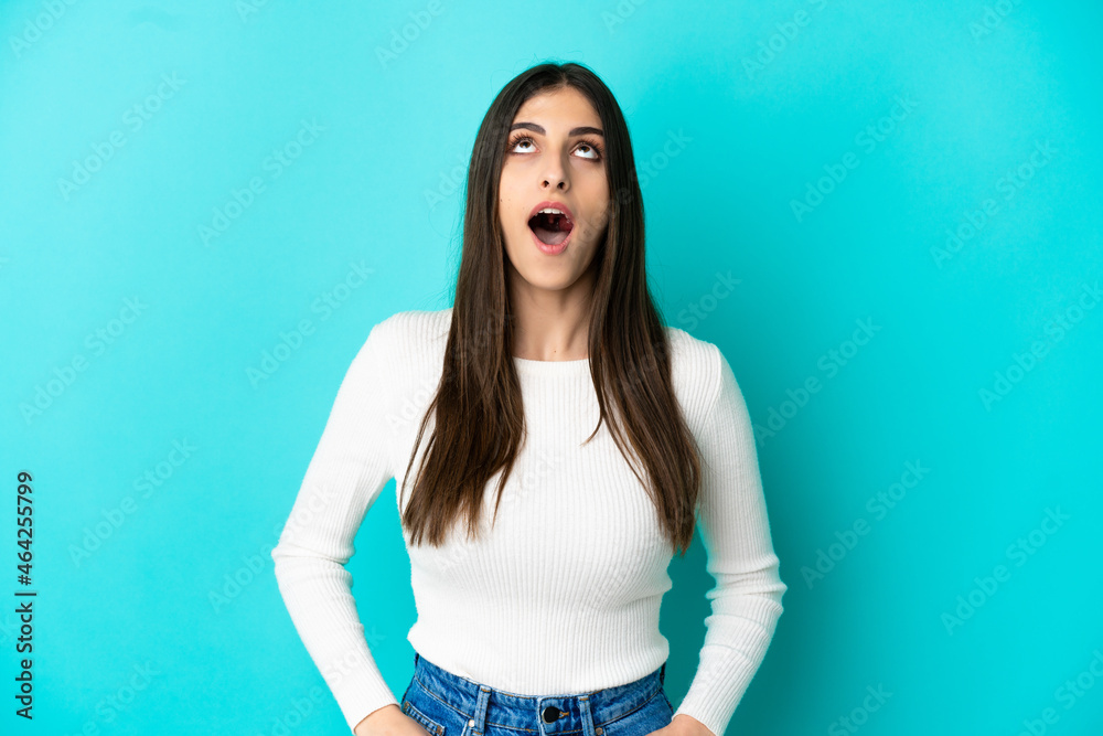 Young caucasian woman isolated on blue background looking up and with surprised expression Young caucasian woman isolated on blue background looking up and with surprised expression