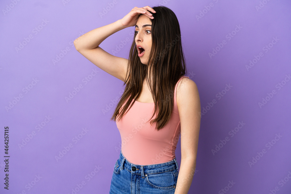 Young caucasian woman isolated on purple background doing surprise gesture while looking to the side Young caucasian woman isolated on purple background doing surprise gesture while looking to the side