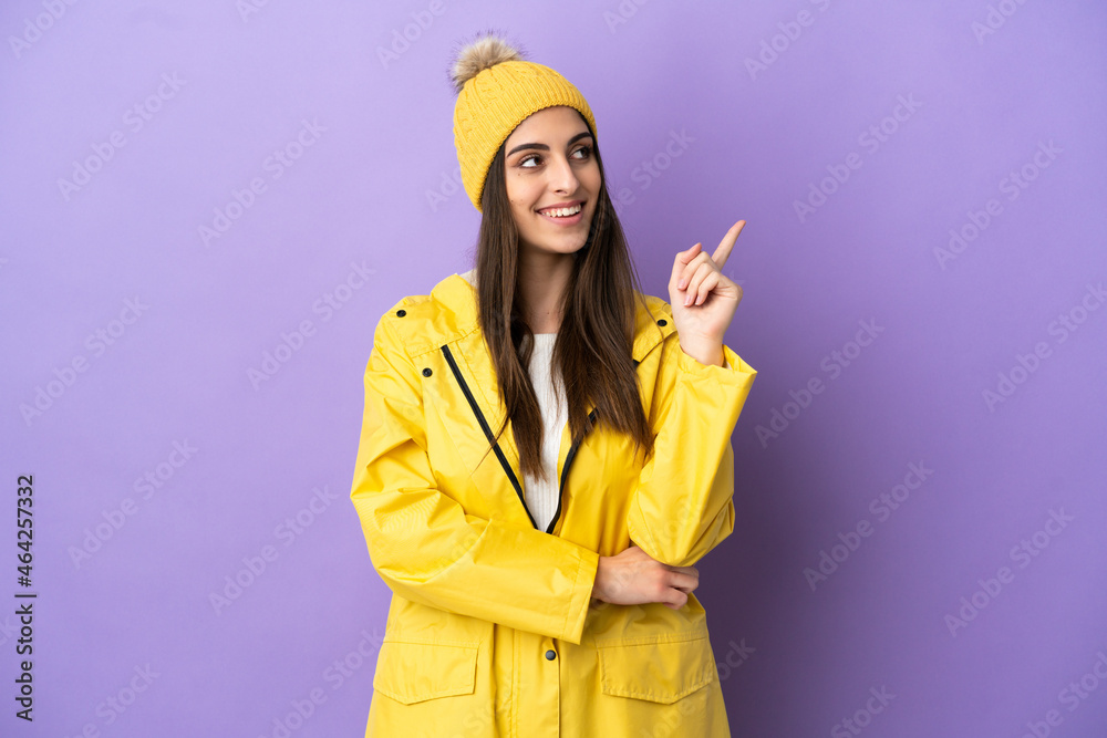 Young caucasian woman wearing a rainproof coat isolated on purple background pointing up a great idea Young caucasian woman wearing a rainproof coat isolated on purple background pointing up a great idea