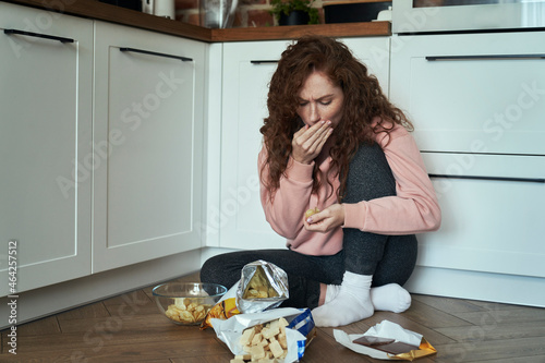 Young caucasian woman eating snacks greedily on the kitchen floor photo