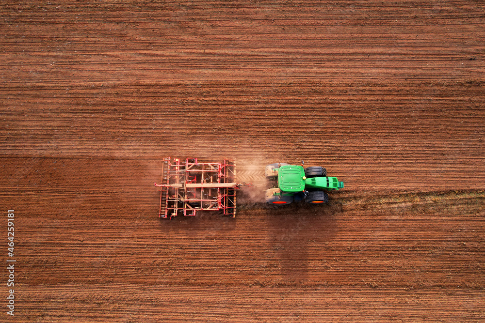 Obraz premium Tractor with disc cultivator Vaderstad on cultivating field. Agricultural tractor with Plough on Plowed and cultivation field. Soil Tillage and sowing seeds. Planting and Seeding Equipment.