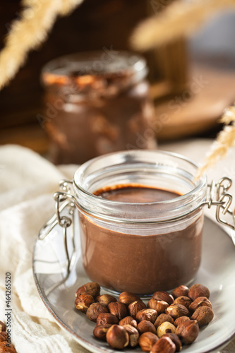 Homemade hazelnut cocoa chocolate cream in mason jar on plate surrounded by hazelnuts