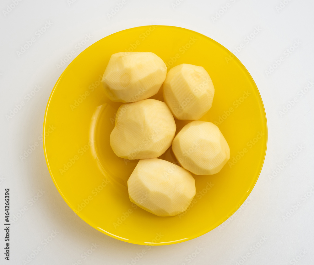 Five fresh peeled potatoes in the yellow plate on white background