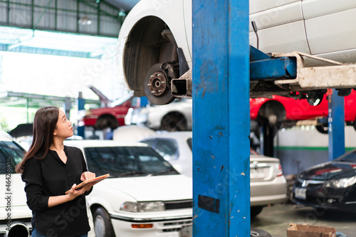 Asian young woman in black shirt examining a vehicle suspension and break system in garage.