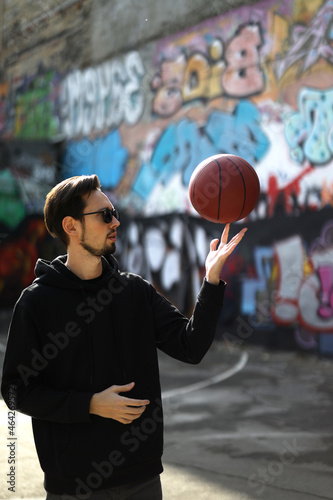 a man plays basketball on a sports platform on the street. young sportsman spinning basketball on his finger © Irina