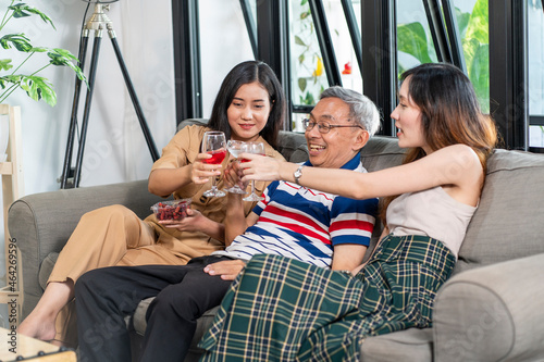 Granddaughter, daughter and grandfather of three generations sitting on the sofa watching TV and celebrating drinks together, having a happy family in the house.  photo