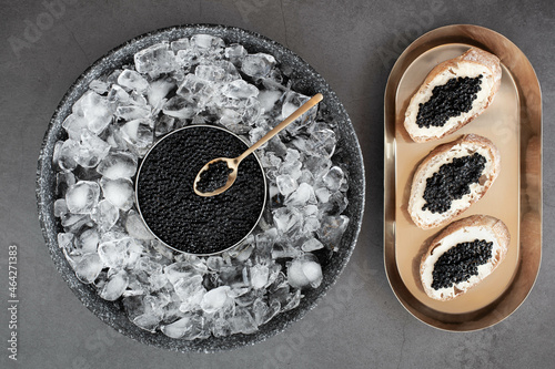 Black caviar in can on ice and bread with butter on golden plate