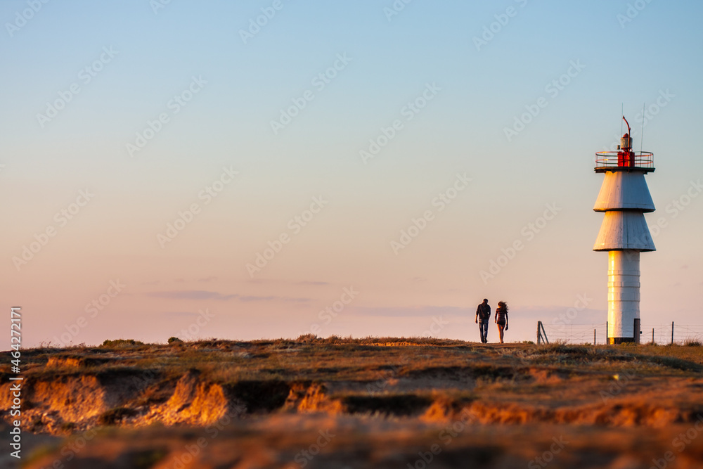 A loving guy and a girl are walking at sunset along the coast, near the lighthouse. Evening, romantic sailing trip.
