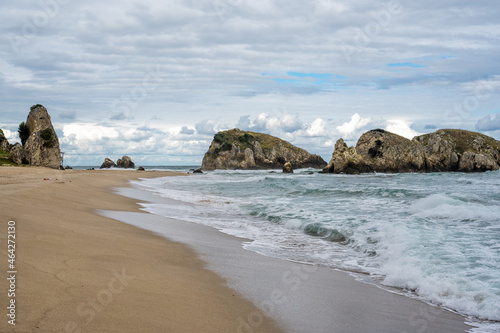 Beautiful sandy ocean beach with large rocks on shore and in the water. Powerful waves on ocean