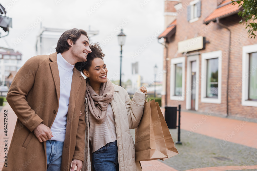 cheerful african american woman holding shopping bags near boyfriend outdoors.