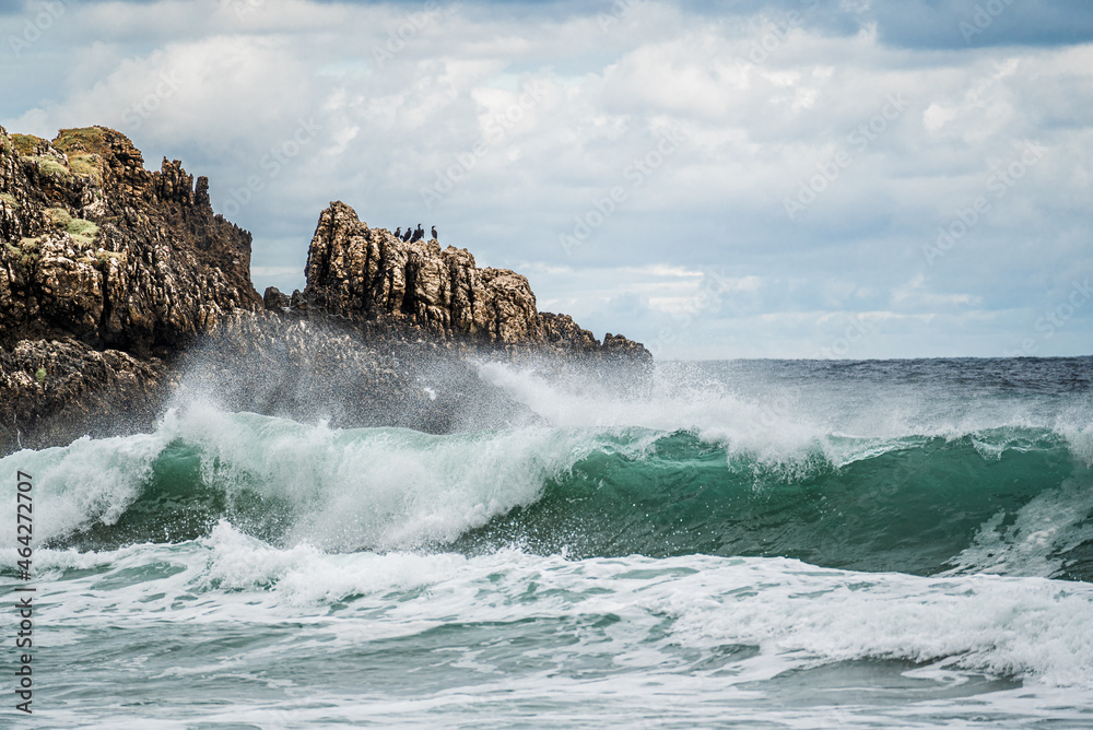 seascape with gloomy sky, sharp rocks and big waves on the sea. Rugged cliffs and swirling sea. Rugged, rocky coastline with white water swirling around the rocks