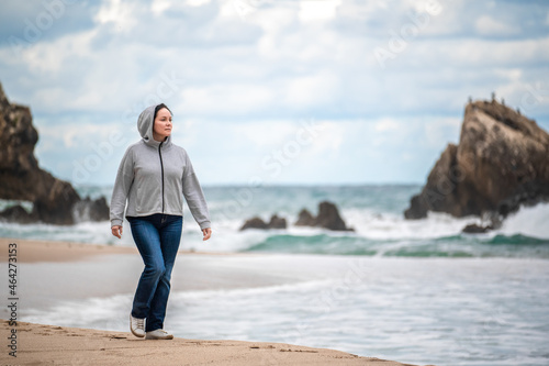 Portrait of happy smiling excited caucasian adult woman in jeans walking running at autumn fall day outdoor on shore beach, lifestyle natural emotion. california coast
