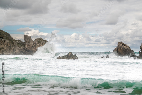 Ocean water splash on rock beach with beautiful sky and clouds. Sea wave splashing on stone at sea shore on winter. Sea waves lash line impact rock on beach