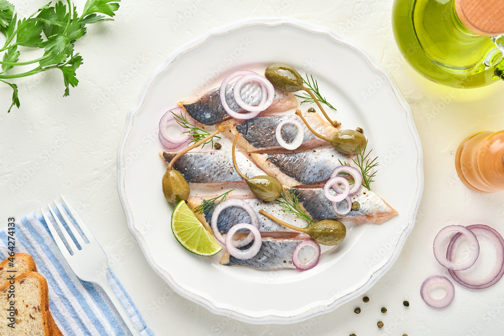 Salted herring with spice, herbs and onion on white plate on light stone background with copy space. Marinated sliced fish. Food with healthy unsaturated fats, flat lay