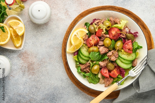Tuna salad with fresh vegetables, olives, capers and lemon served in bowl on light grey background. Top view with copy space.