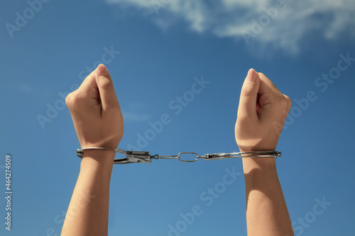 Woman in handcuffs against blue sky, closeup
