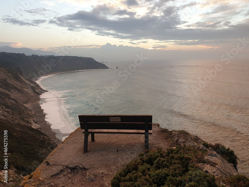 Shot of a wooden bench on a rocky formation above a coastline during sunset photo