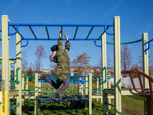 Carefree girl having fun while hanging on monkey bars while playing in the park in sunny autumn day