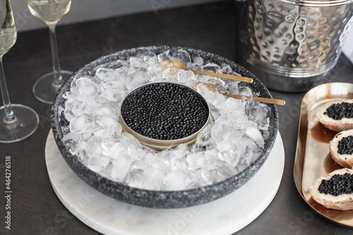 Black caviar in can on ice, caviar sandwich on golden plate, champagne in glass